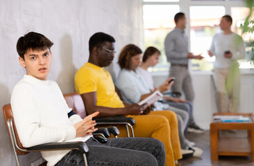 Emotional young guy sitting in lobby of government agency with indignant expression, waiting for clerk consultation..