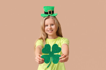 Cute little girl in leprechaun hat with clover on brown background. St. Patrick's Day celebration
