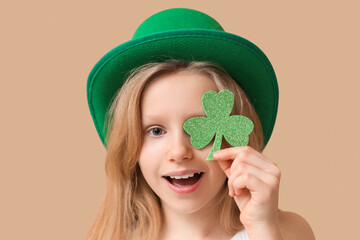 Cute little girl in leprechaun hat with clover on brown background. St. Patrick's Day celebration