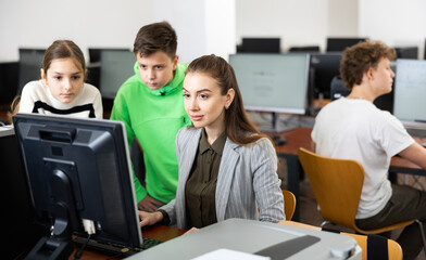 Obraz premium Teacher explaining task solution to young girl and boy during computer science lesson in school.