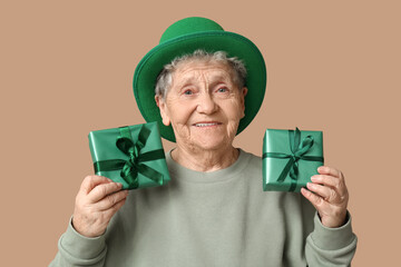 Senior woman in leprechaun hat with gift boxes on brown background. St. Patrick's Day celebration