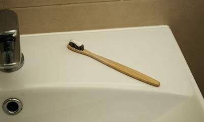 Toothbrush wooden handle. Toothpaste on bristles. White ceramic sink. Bathroom hygiene concept.

