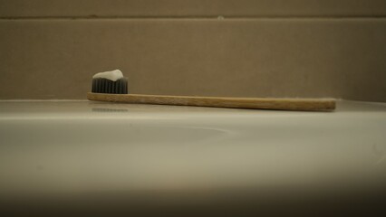 Toothbrush wooden handle. Toothpaste on bristles. White ceramic sink. Bathroom hygiene concept.

