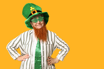Senior woman in leprechaun hat and decorative glasses with red beard on yellow background. St....
