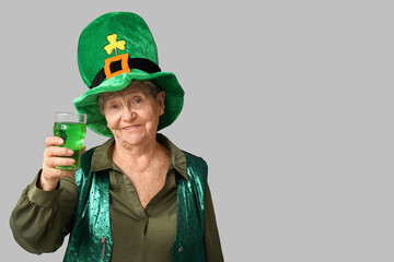 Senior woman in leprechaun hat with glass of beer on grey background. St. Patrick's Day celebration