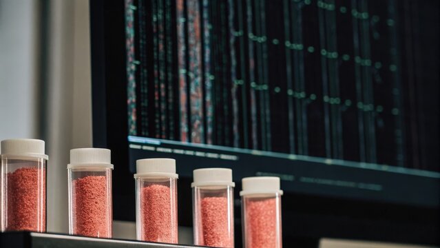 A series of labeled vials containing genetically modified samples displayed against a backdrop of hightech software running genetic sequencing algorithms on a nearby monitor.