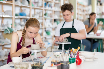 Teenage boy and teenage girl students in apron make clay product in ceramic workshop