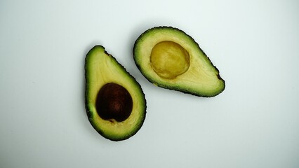 Halved avocado fruit. Seed exposed center. Smooth green flesh. White studio background.