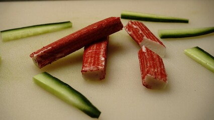 Crab sticks layout. Sliced cucumber pieces. White cutting board. Sushi ingredient concept.

