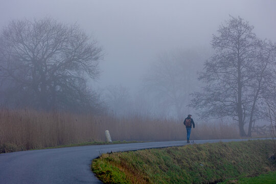 Hiking concept, Back view of a dutch man walking on the dike with mist and foggy in the morning, Countryside road along the river that can dimly seen, Hobby and leisure activity in winter, Netherlands