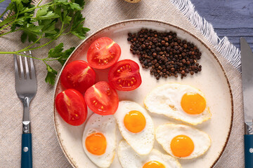 Plate with fried quail eggs, tomatoes, peppercorns and cutlery on table, closeup
