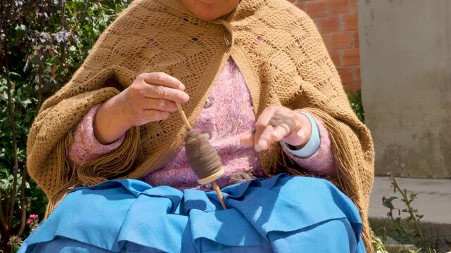 slow motion of hands of a third age woman of aymara culture with skirt spinning wool in a handmade way in the backyard of her house in the city of la paz, Bolivia - concept of craftsmanship