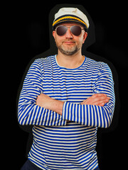 Portrait of a sailor in blue and white stripes shirt and captain hat. Male in his 40s with grey beard and dark glasses, hands crosses, smile on his face. Ocean theme party clothes.
