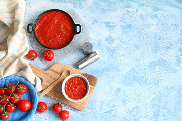 Bowl and frying pan of tomato sauce on blue background