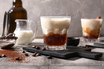Glasses of White Russian cocktail with coffee beans and jug of cream on grey tile table