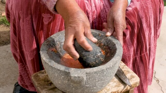 hands of old woman of the aymara chola culture grinding in a mortar or also called batan in the courtyard of her house in la paz, bolivia - cooking concept
