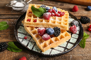 Plate of sweet Belgian waffles with different fresh berries and mint on wooden background