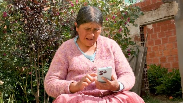 Cholita adult woman in pollera holding her cell phone in the courtyard of her home in La Paz, Bolivia - concept of older adults