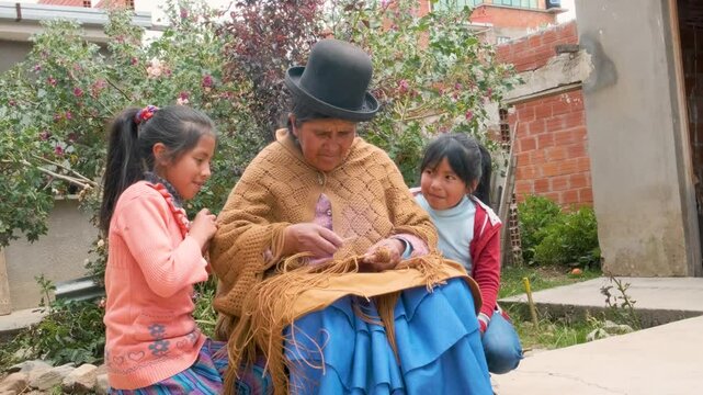adult aymara woman in pollera working on handcrafted wool textiles with her granddaughters at home - work concept