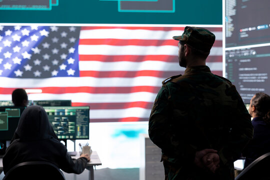 American military personnel supervising cyber warfare activity in high tech office, examine top secret intelligence on big screen. Governmental experts manage hybrid war, digital conflict prevention.