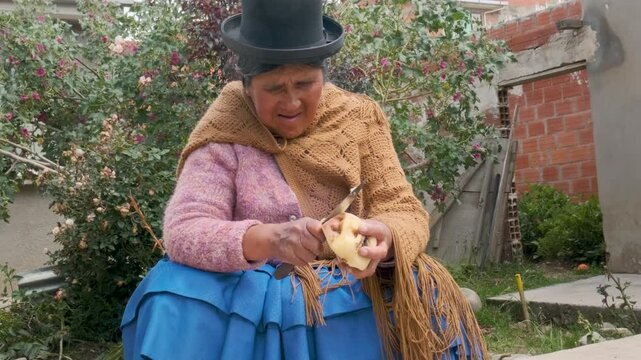 old cholita woman in pollera peeling potatoes with a knife in the backyard of her house - housework concept