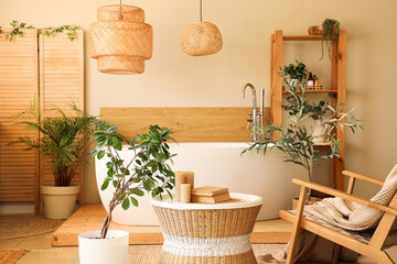Interior of comfortable bathroom with coffee table, bathtub, houseplant and armchair