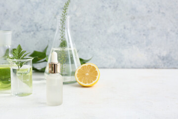 Bottle of oil, laboratory glassware with samples and ingredients for preparing natural cosmetics on white table near grunge wall