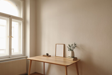 Mediterranean living room. Blank picture frame mockup. Vase with olive branches. Cup of coffee, tea on wooden. Parquet floor. Home office table at window. Minimal Scandi interior. Beige wall