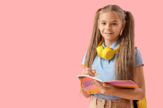 Cute little girl writing something in notebook on pink background