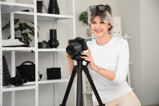 Beautiful young happy female photographer with professional camera taking photo in studio - Powered by Adobe