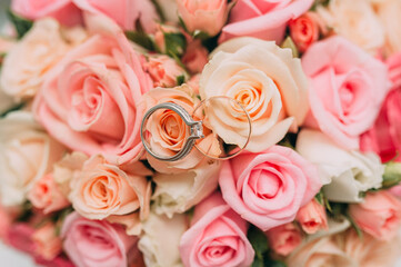 Close-up of wedding rings placed on a bouquet of pink roses, showcasing the elegance of the rings and flowers.