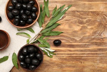 Bowls with tasty black olives and leaves on wooden background
