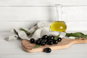 Board with tasty black olives on white wooden background