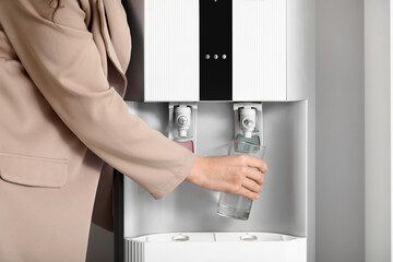 Young businesswoman pouring cold water from cooler in office, closeup