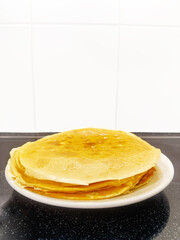 Stack of Thin Homemade Crepes with Golden Butter Glaze. High quality photo A delicious stack of thin, golden crepes with a buttery glaze, freshly made and served on a white plate. These homemade