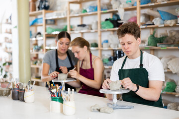 Young man in apron modeling clay pottery in workshop