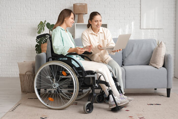 Young woman in wheelchair and her friend using laptop at home