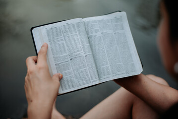 A Bible held in someone's hands with a peaceful lake in the background, symbolizing faith and reflection."