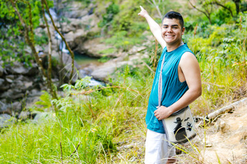 Young colombian backpacker exploring tropical waterfall in lush green forest