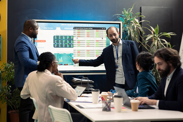 Team of business workers reviewing statistics and infographics on interactive board, joining forces...