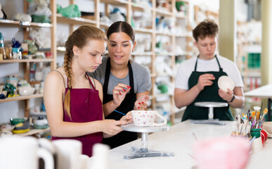 Woman master potter teaches teen girl how to draw and glaze pottery