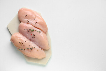 Board with raw chicken breast, thyme and peppercorns on white background