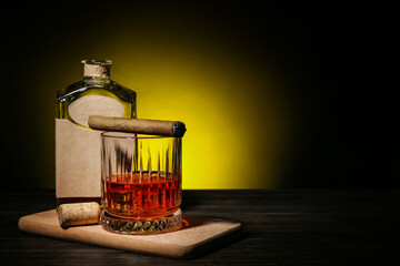Bottle and glass of rum with cigar on wooden table against dark background