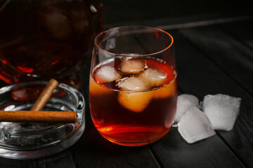 Glass of rum with ice cubes and cigars on black wooden background