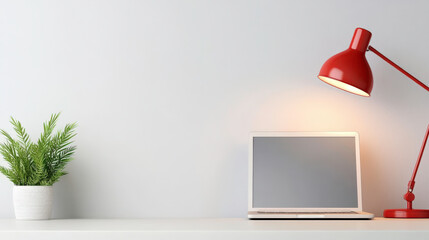 Cozy workspace setup featuring a modern laptop with a red desk lamp, indoor plant, and minimalistic design elements on a soft gray background