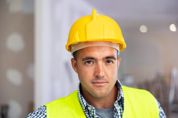 Portrait of man builder in yellow vest and helmet standing in apartment during repair works.