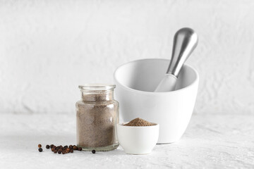 Jar of black pepper powder with peppercorns, mortar and pestle on white background