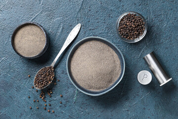 Bowls of black pepper powder and spoon with peppercorns on dark background