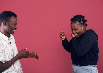 A young man and woman share a joyful moment, laughing as she playfully covers part of her face....