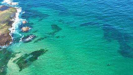 Drone shot aerial view of a reef with clear blue and turquoise water near a beach in Australia 
